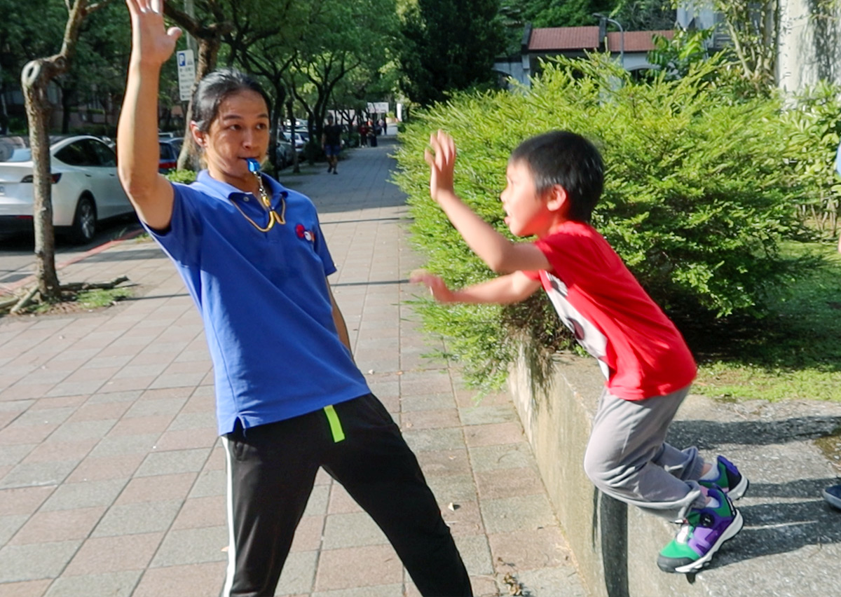 專業體能教練在戶外步道與孩童進行擊掌互動與指令訓練，透過趣味化引導提升反應力與大肌肉發展。