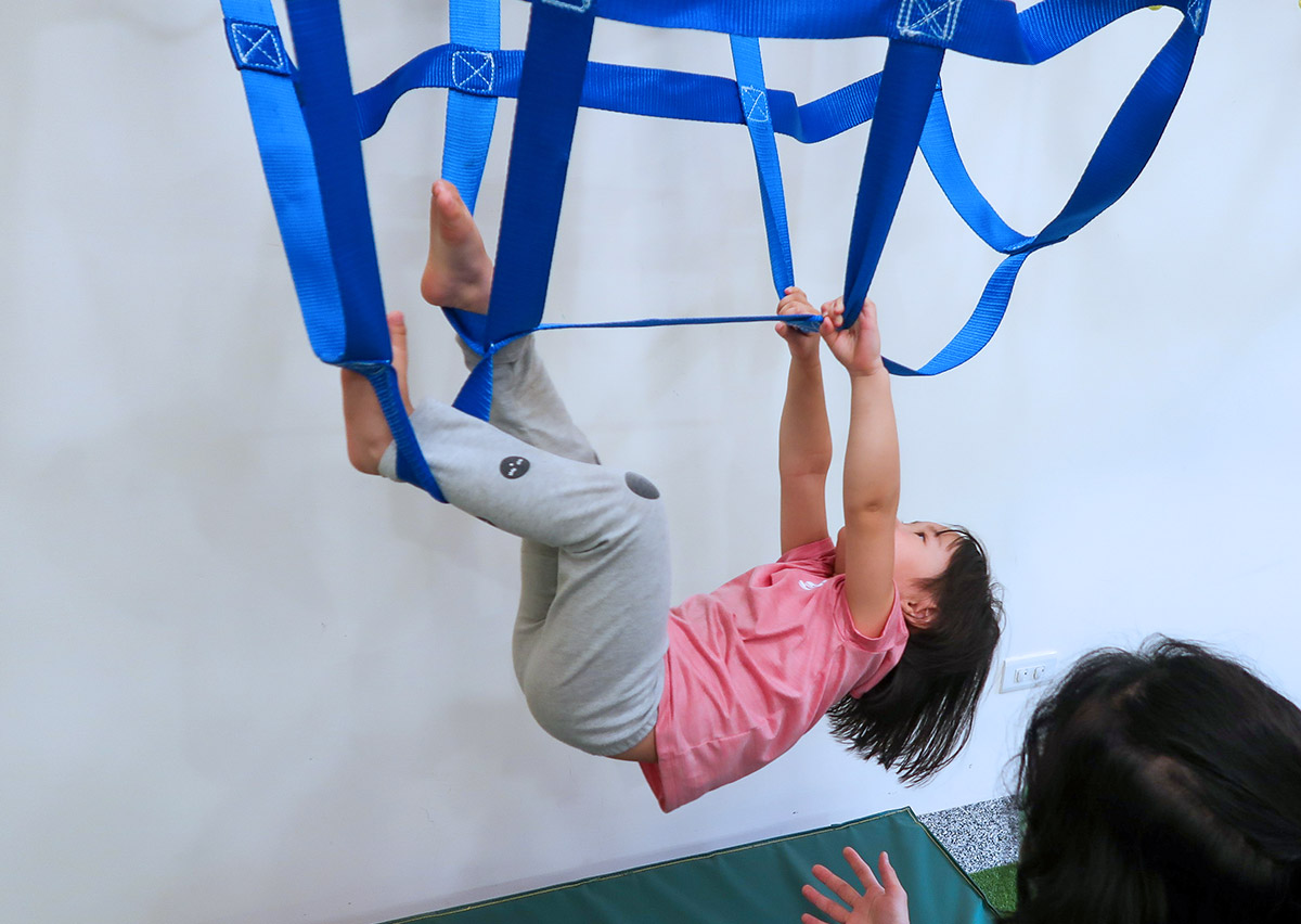 幼齡學員在 Oovi 專業教練看顧下，利用藍色懸吊教具練習抓握與支撐，在趣味遊戲中發展肢體力量與空間定位知覺。