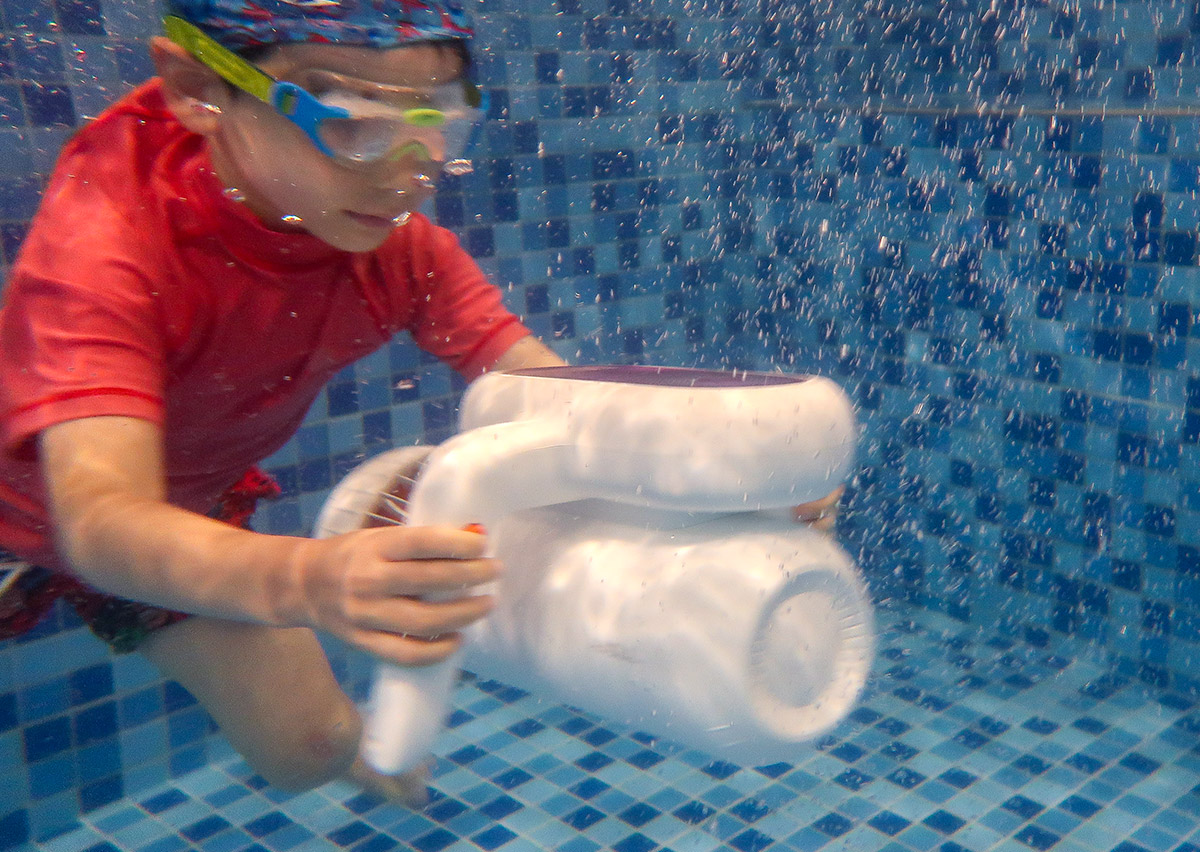 學童在泳池中使用白色水下推進器（DPV）滑行，結合科技器材增加游泳課趣味性並降低對深水的恐懼。