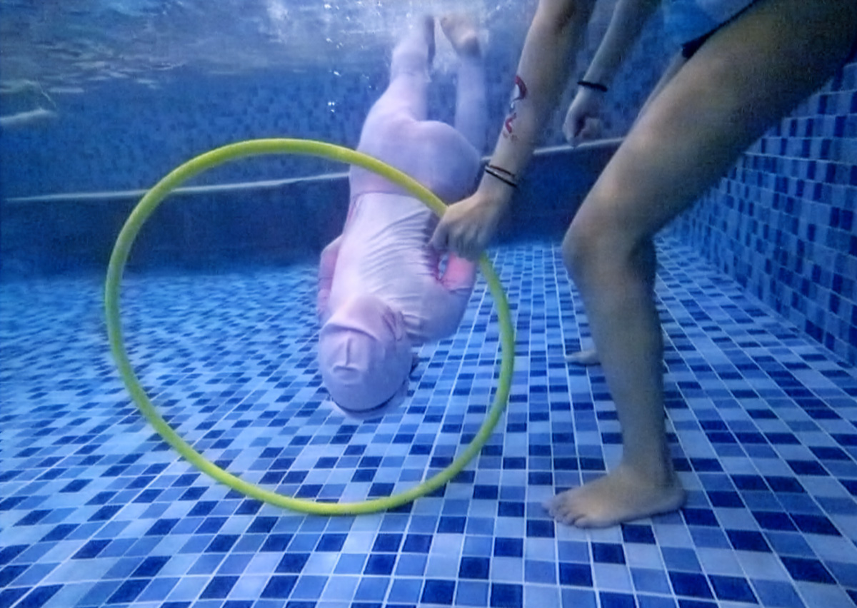 兒童在水中靈活地鑽過黃色呼拉圈,這項水中障礙 (Underwater Obstacle) 挑戰能訓練身體的柔軟度、閉氣技巧與空間感,是進階游泳課程中有趣的關卡設計。