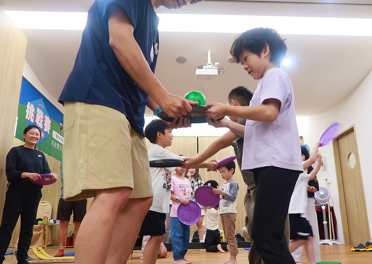 兒童排隊進行物品傳遞的親子平衡挑戰賽,訓練手眼協調與反應速度,並在遊戲過程中學習團隊合作 (Teamwork) 與輪流等待的社交規範。