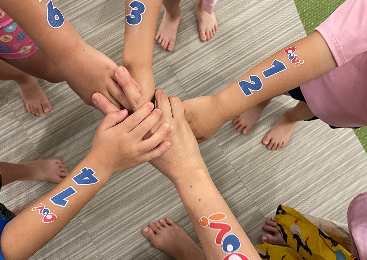 參加活動的兒童們伸出手臂圍成圓圈,手臂上貼著數字與 Oovi logo 的紋身貼紙,象徵團隊精神 (Team Spirit) 與歸屬感。這類團體儀式感能有效促進孩子的同儕互動 (Peer Interaction) 與社交能力發展。