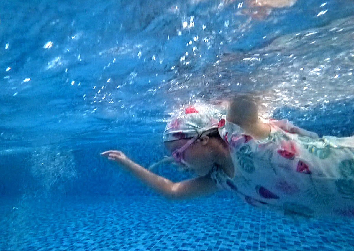 女童在水中呈現標準的流線型 (Streamline) 滑行姿勢,配戴泳鏡睜眼展現極佳水性。這張照片體現了游泳課程中降低水阻與身體控制的教學成果。