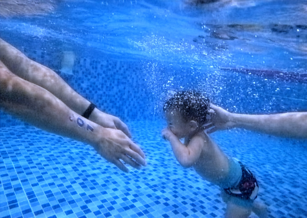 兒童在水中進行潛水練習並游向教練伸出的雙手,這畫面象徵教學過程中的信任感 (Trust) 與安全引導。透過漸進式的閉氣訓練與目標設定,幫助孩子克服恐懼,享受自在的水中悠游。