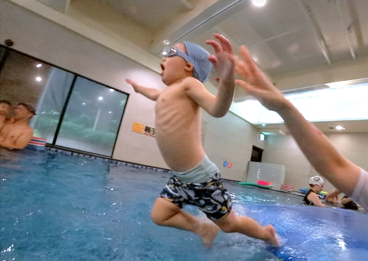 幼兒張開雙手興奮地跳入水中,游向等待的家長與教練。這瞬間捕捉了孩子克服高度恐懼的勇氣 (Courage),以及對水中環境與陪伴者的信任感,是游泳自救課程中的重要里程碑。