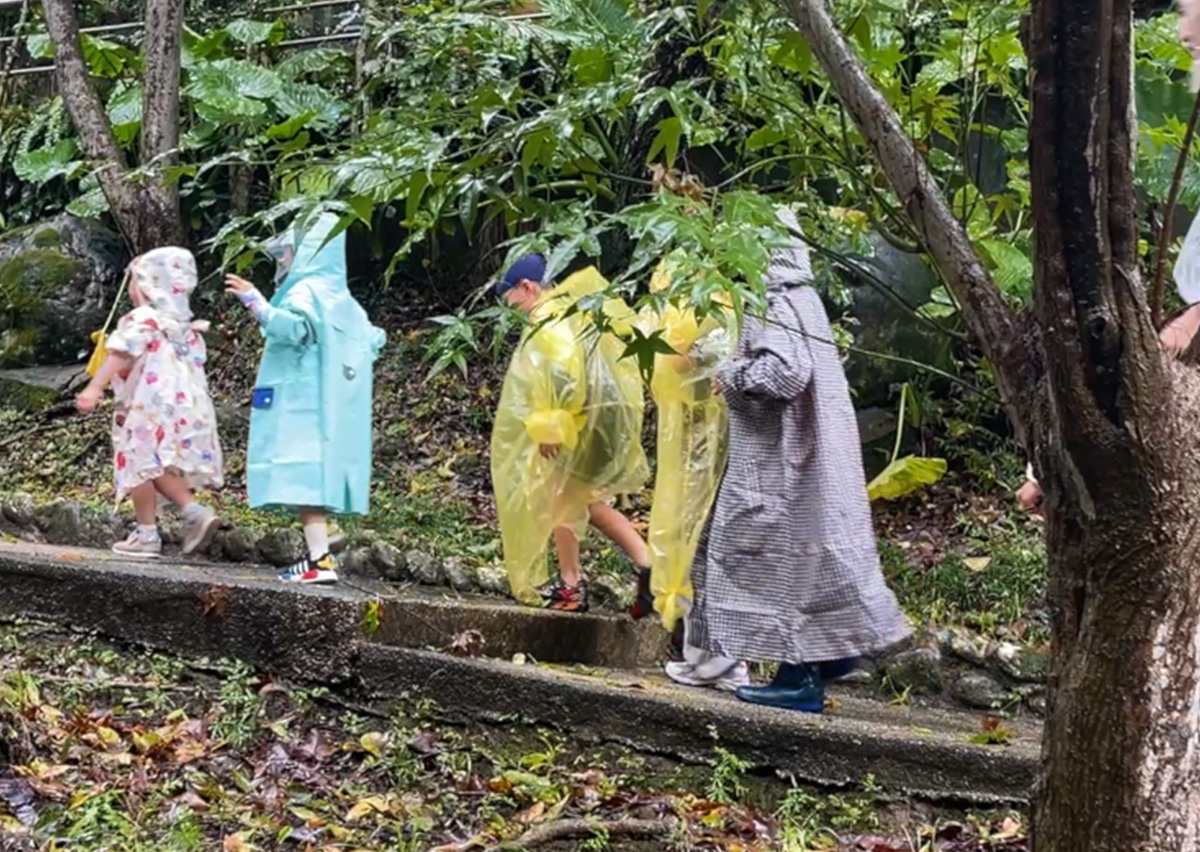 一群穿著雨衣的孩子在教練帶領下進行水陸挑戰賽的路跑部分,不畏雨天走在自然步道上。這象徵 Oovi 課程重視培養孩子的環境適應力 (Resilience) 與親近自然的感官體驗。