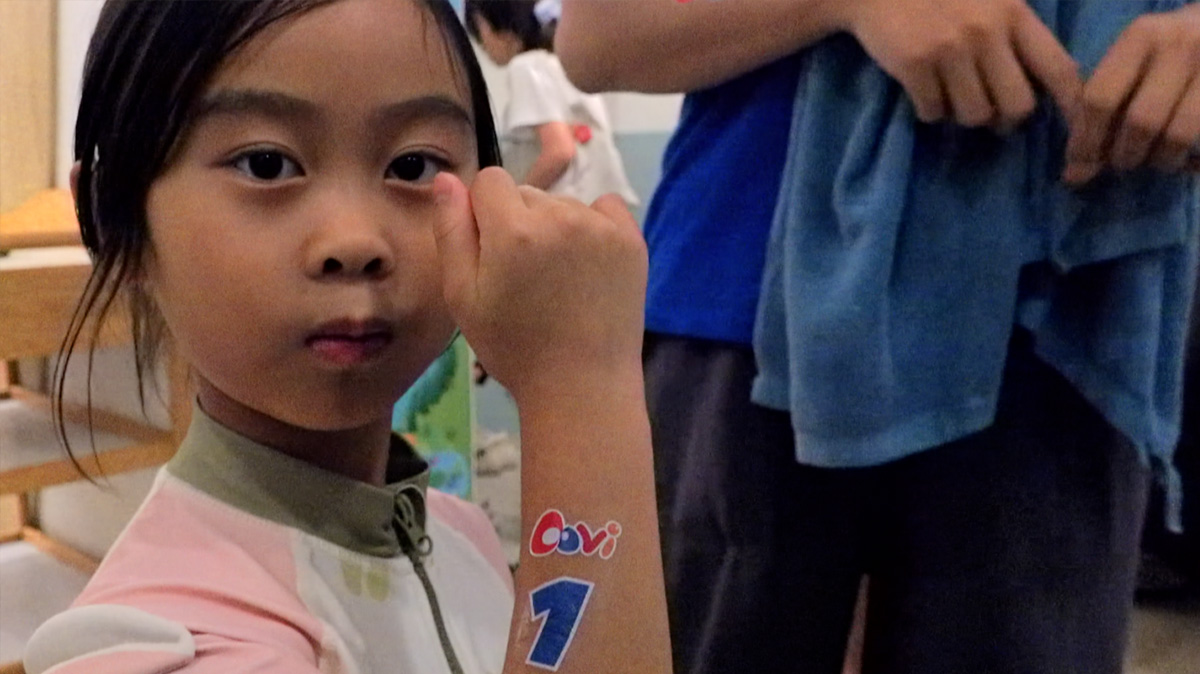 女童自信展示手臂上的 Oovi 品牌貼紙與參賽號碼 "1"，眼神充滿堅定。這象徵著參與活動建立的身份認同 (Identity) 與運動家精神，是品牌社群凝聚力的最佳展現。