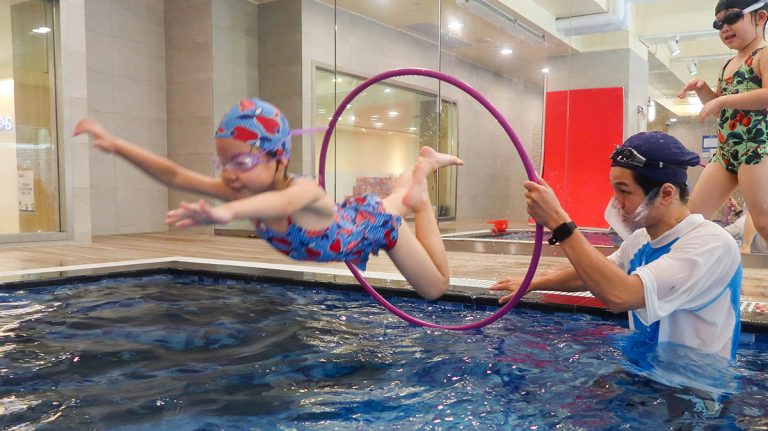 Oovi 暑假營隊學員在教練守護下,精準躍過水中圓環障礙,透過挑戰遊戲提升空間判斷力與水域勇氣。