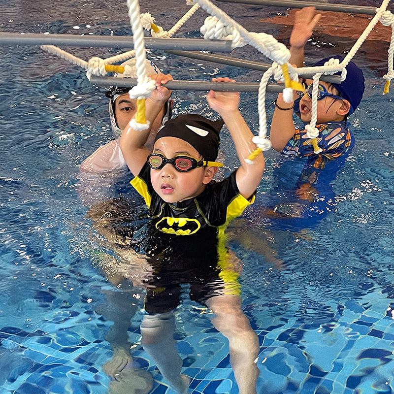 孩子在教練協助下挑戰水上繩梯，這項運動能訓練上肢抓握力與全身協調，讓孩子在水中環境也能精確控制肢體動作。