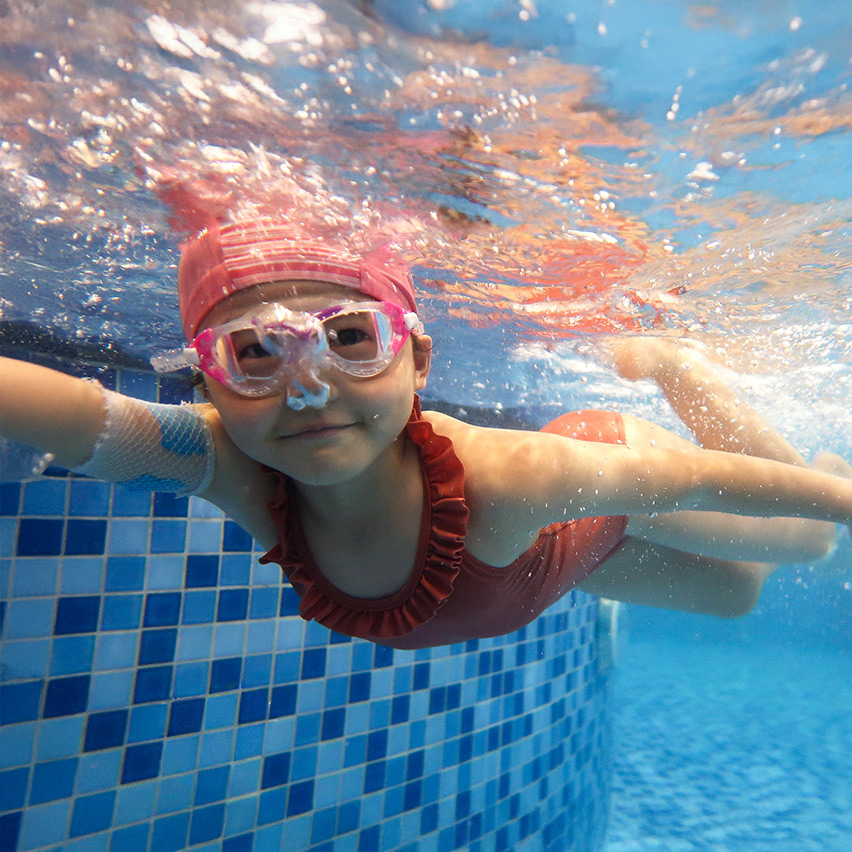 兒童佩戴泳鏡在水中自信潛水並直視鏡頭，展現良好的水下閉氣與環境適應力，是參加進階水上挑戰賽前的必備水性基礎。